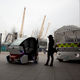 A woman poses for photographers beside a prototype driverless car called a LUTZ (Low-carbon Urban Transport Zone) Pathfinder Pod, center, and a Meridian shuttle, right, during a launch event for the media near the O2 Arena in London